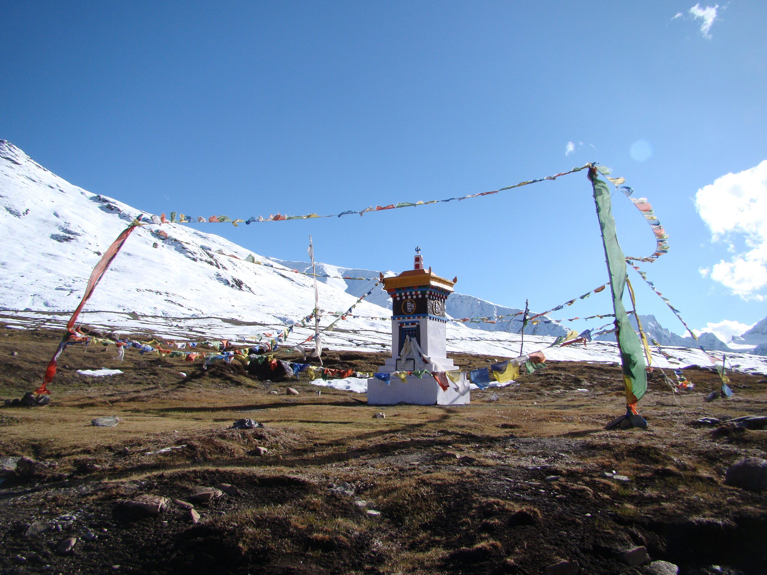 Snow-covered Himalayan mountains and colorful prayer flags surrounding a small shrine in India