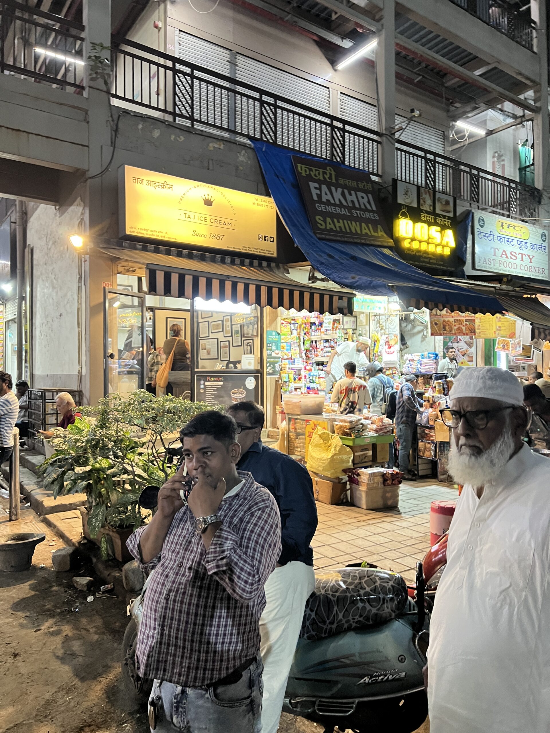 Man speaking on a mobile phone outside illuminated shops on a busy street in Mumbai